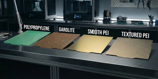 Comparison of glass, textured PEI, and Garolite 3D printer build surfaces on a workbench.